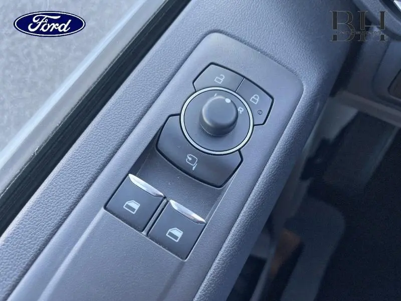 Gros plan sur les commandes de réglage des rétroviseurs et vitres côté conducteur du Ford Transit Custom Fourgon gris Matter 2025.