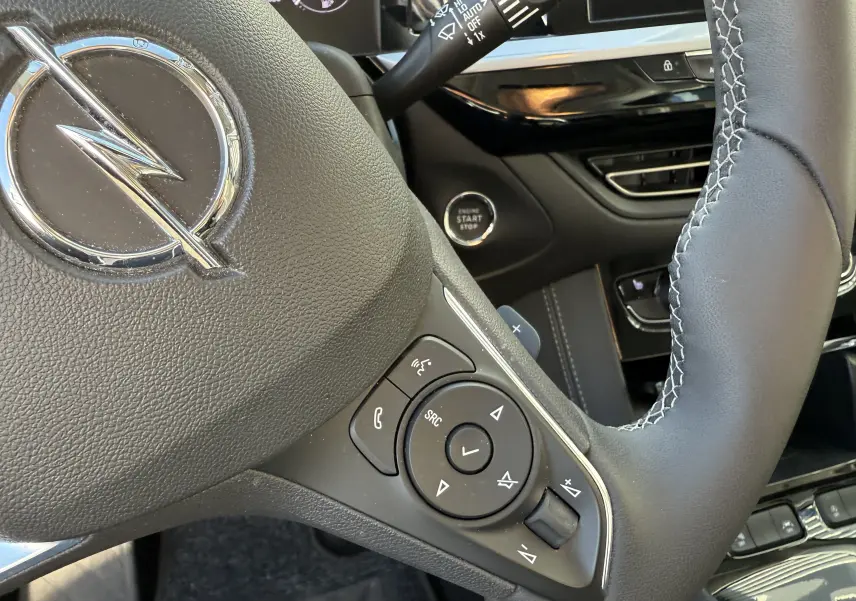Gros plan sur le volant en cuir noir avec logo Opel et commandes intégrées du tableau de bord du Grandland gris Artense.