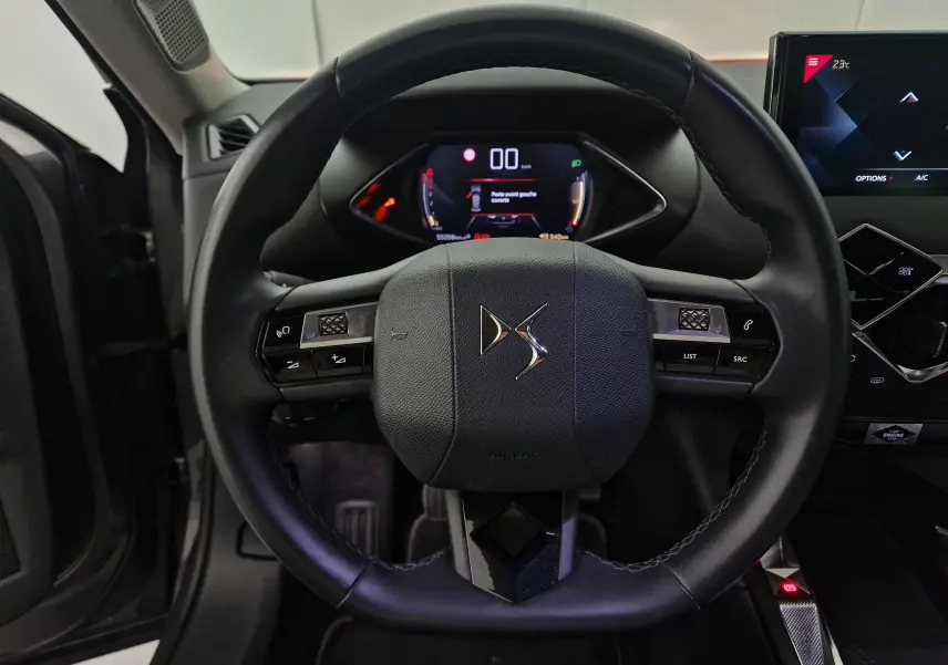 Vue frontale du volant noir du DS3 Crossback 2022 avec commandes intégrées et tableau de bord numérique allumé.