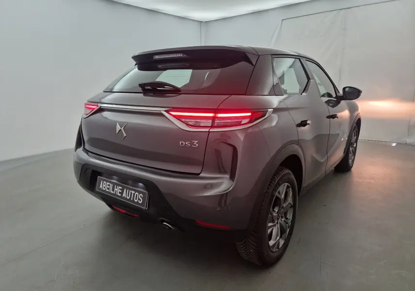 Vue 3/4 arrière droite d'un DS3 Crossback gris platinium avec feux arrière allumés dans un studio.