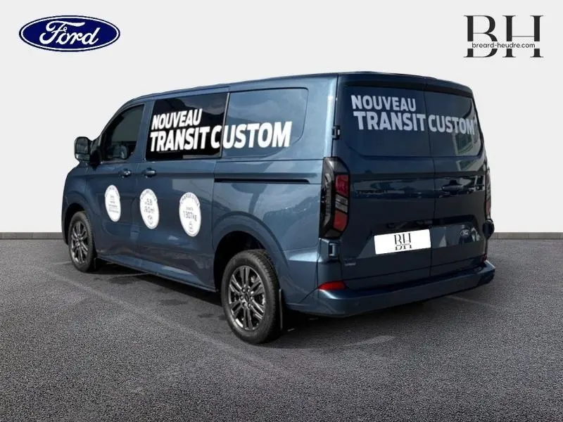 Vue 3/4 arrière droite du Ford Transit Custom bleu azur métallisé avec marquages publicitaires blancs sur les vitres latérales et arrière.