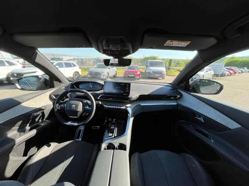 Intérieur du Peugeot 5008 2024 en gris, vue avant du poste de conduite avec volant compact et écran tactile central.