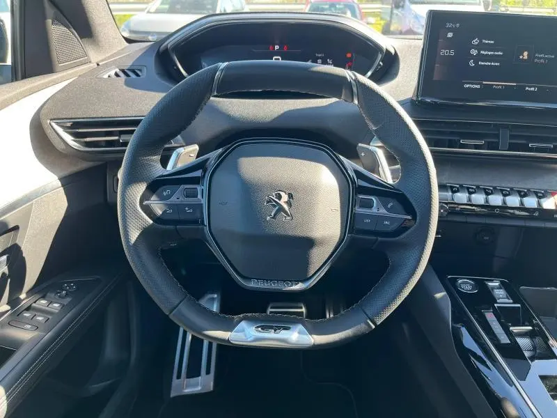 Vue rapprochée du volant cuir noir multifonction du Peugeot 5008 gris 2024 avec tableau de bord numérique et écran tactile.