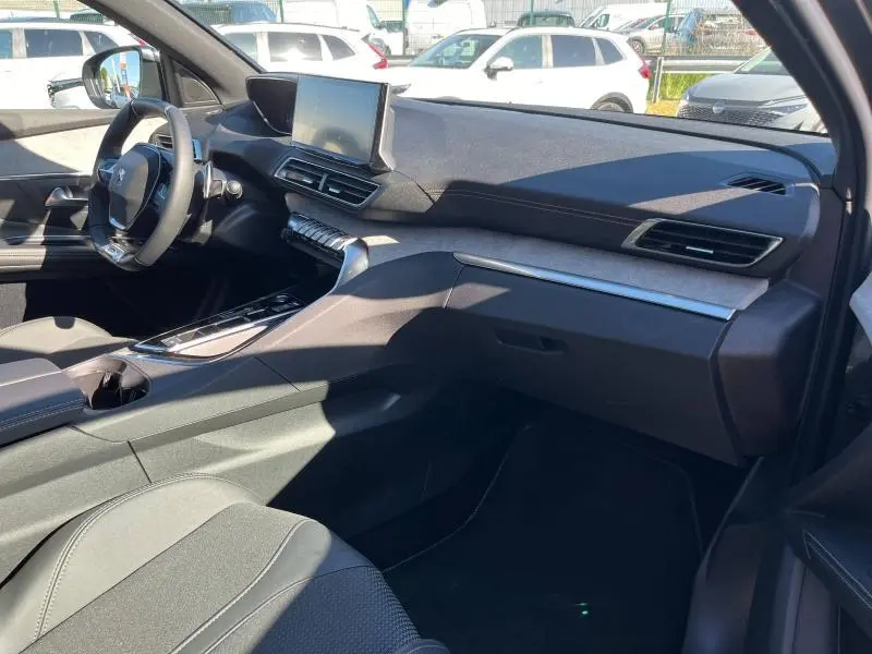 Intérieur avant droit du Peugeot 5008 gris 2024, tableau de bord moderne avec écran tactile et inserts carbone.