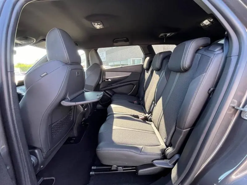 Vue intérieure côté droit de la banquette arrière en tissu noir du Peugeot 5008 gris, avec tablette rabattable au dos du siège avant.