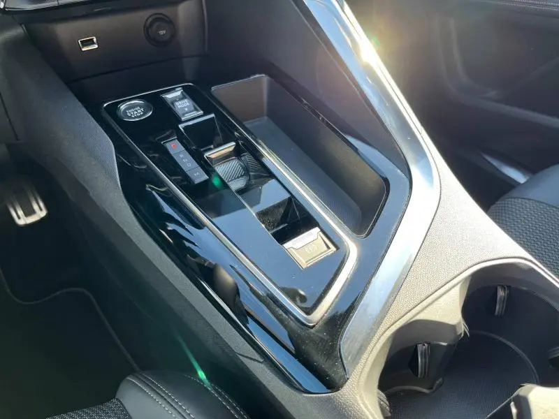 Gros plan sur la console centrale noire brillante du Peugeot 5008 2024 avec boîte auto et bouton start/stop.