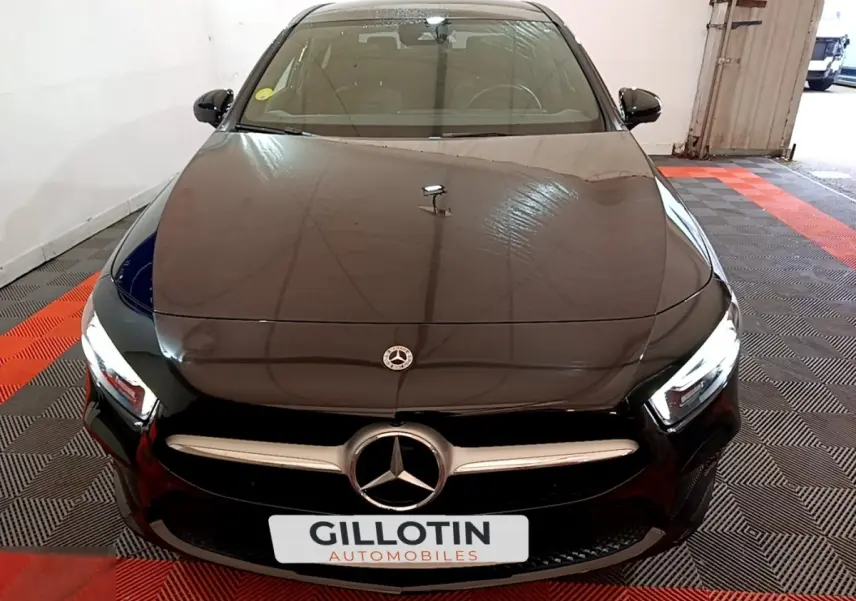 Vue avant d'une Mercedes Classe A berline noire avec calandre chromée et phares LED allumés dans un garage.