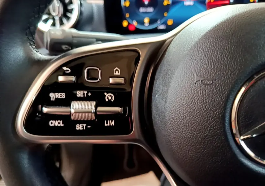 Gros plan sur la partie gauche du volant cuir noir d’une Mercedes Classe A 2022 avec commandes de régulateur de vitesse et affichage numérique en arrière-plan.