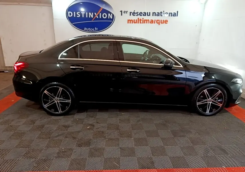 Vue latérale droite d'une Mercedes Classe A Berline noire 2022, avec jantes alliage et vitres teintées, en intérieur showroom.