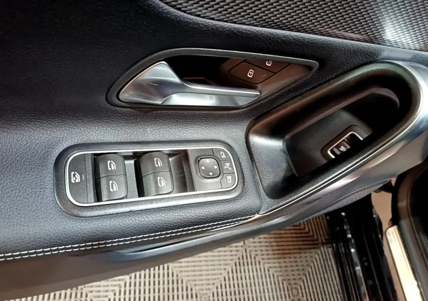 Détail de la porte avant gauche noire de la Mercedes Classe A 2022 avec commandes des vitres et poignée argentée.