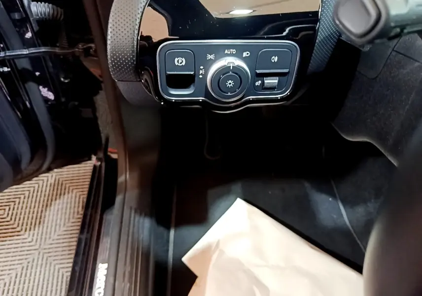 Vue intérieure côté conducteur de la Mercedes Classe A noire, avec commande des feux et frein à main électrique.