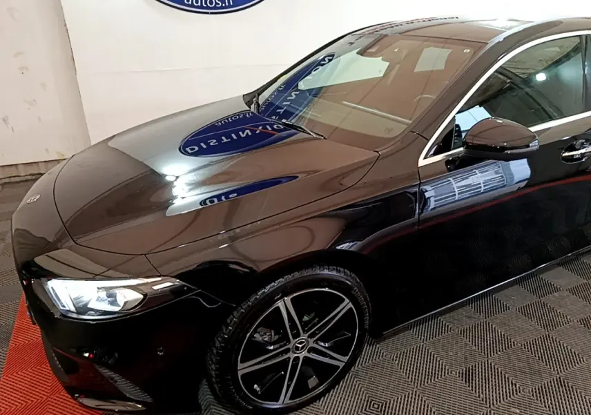 Vue 3/4 avant droite d'une Mercedes Classe A berline noire avec jantes alliage et phares LED allumés.