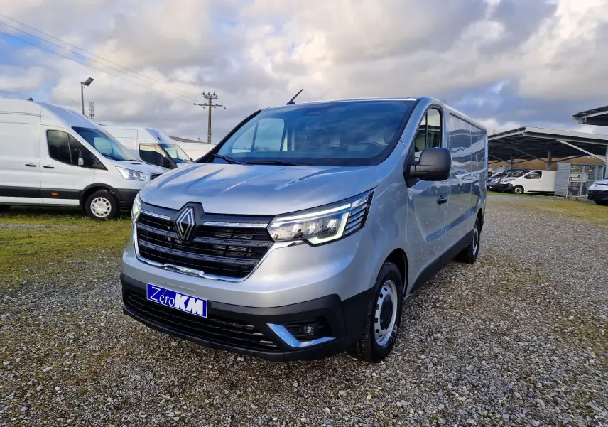 Renault Trafic Fourgon gris Highland en 3/4 avant droit, avec calandre noire et feux LED allumés, sur parking extérieur.