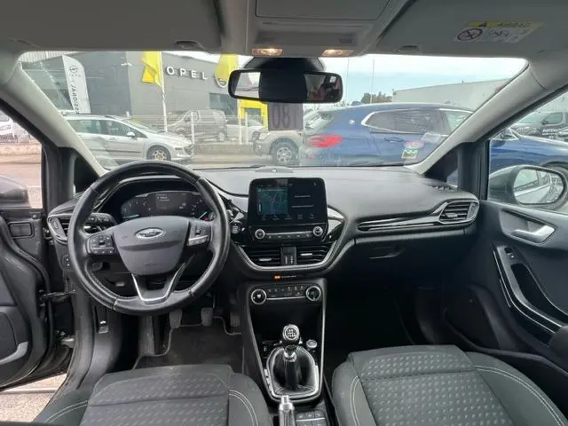 Vue intérieure avant de la Ford Fiesta gris 2018, tableau de bord moderne avec écran tactile et boîte manuelle visible.