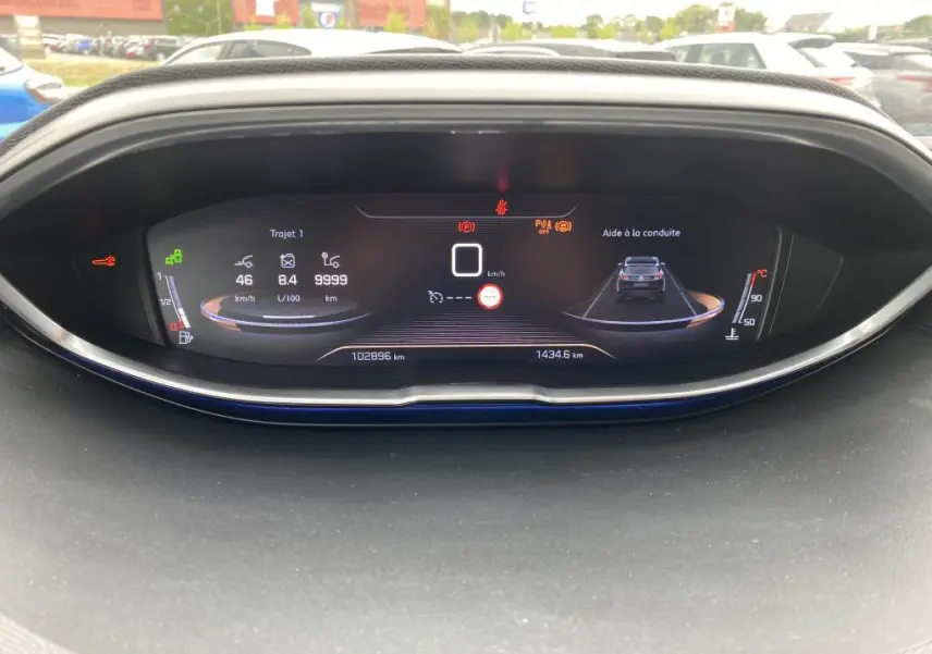 Affichage numérique du tableau de bord du Peugeot 3008 blanc, montrant l'aide à la conduite et les indicateurs de vitesse et consommation.