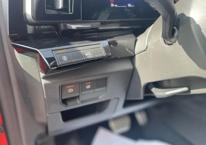 Détail intérieur côté gauche du tableau de bord du Renault Rafale 2025 rouge, avec commandes électroniques et pédalier visible.