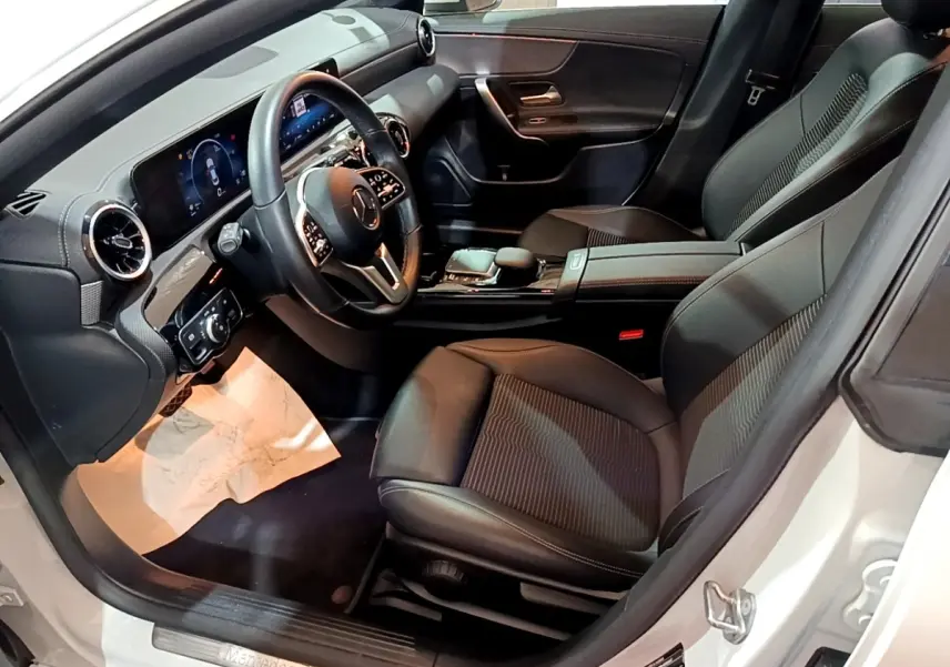 Vue intérieure côté conducteur de la Mercedes CLA 200 d Business Line blanche, avec tableau de bord digital et sièges noirs.