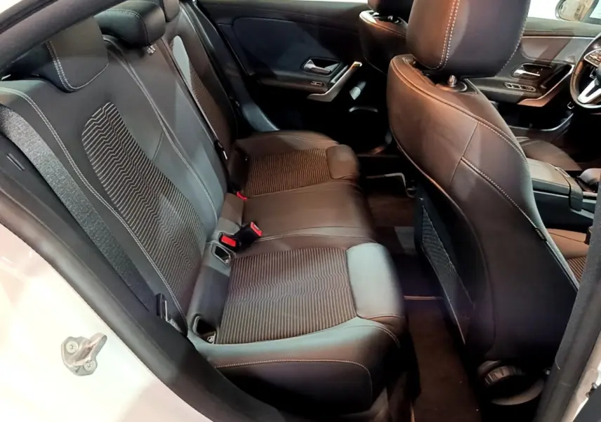 Vue intérieure côté arrière gauche de la Mercedes CLA 200 d Business Line blanche, sièges arrière en cuir noir avec surpiqûres.