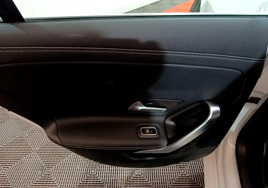 Vue intérieure du panneau de porte avant gauche noir avec poignée alu et bouton de verrouillage, Mercedes CLA 200 d blanc.