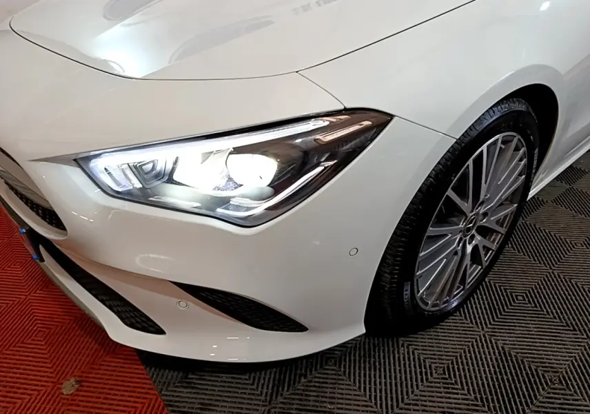 Gros plan sur l’avant droit blanc d’une Mercedes CLA 200 d avec phare LED allumé et jante alliage multibranches.