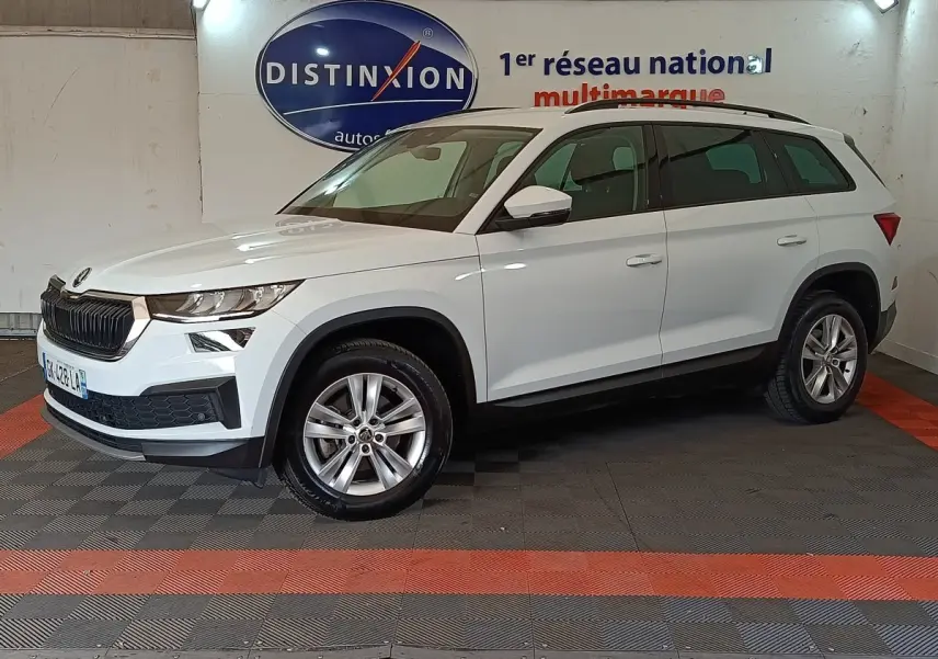 Vue de profil droit d'un Skoda Kodiaq blanc 2022 dans un showroom, avec jantes alliage et barres de toit noires.