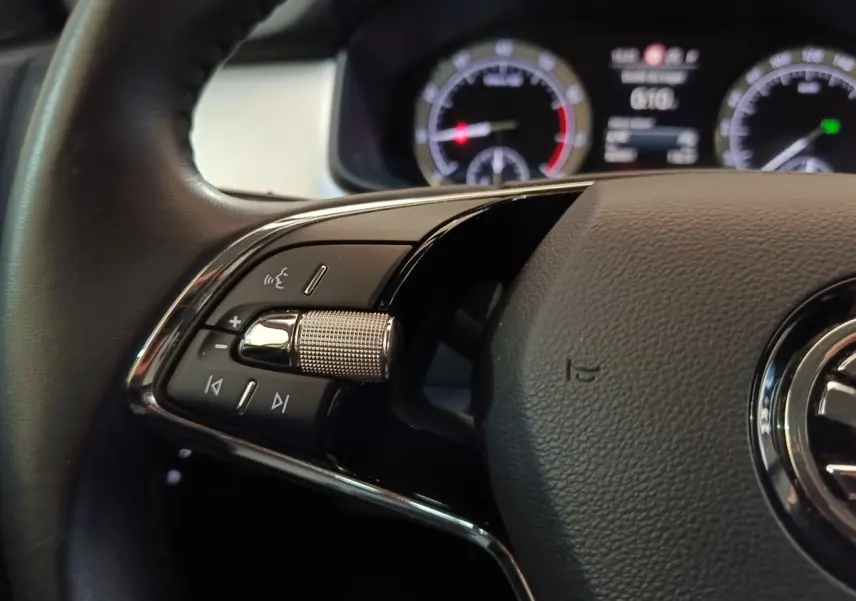 Gros plan sur la partie gauche du volant noir du Skoda Kodiaq 2022 avec commandes audio et affichage digital en arrière-plan.