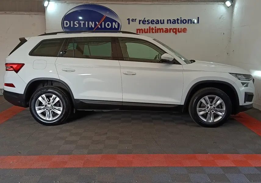 Vue de profil côté gauche d'un Skoda Kodiaq blanc 7 places, version Ambition, dans un showroom multimarque.