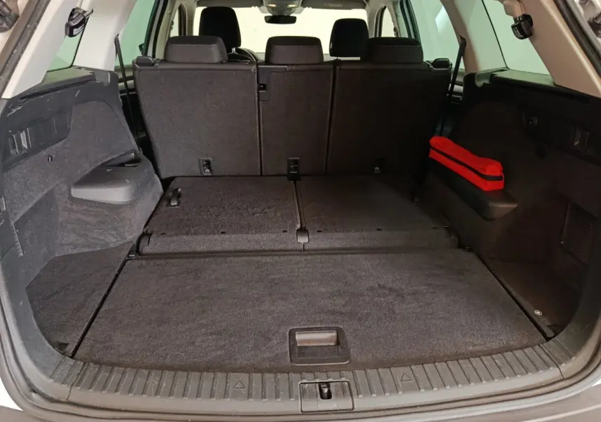 Vue arrière du coffre spacieux du Skoda Kodiaq blanc 2022 avec sièges rabattus et trousse de secours rouge sur le côté droit.