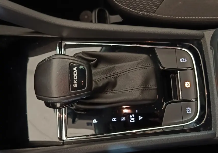 Gros plan sur la commande de boîte automatique noire avec logo ŠKODA, entourée de boutons de contrôle éclairés.