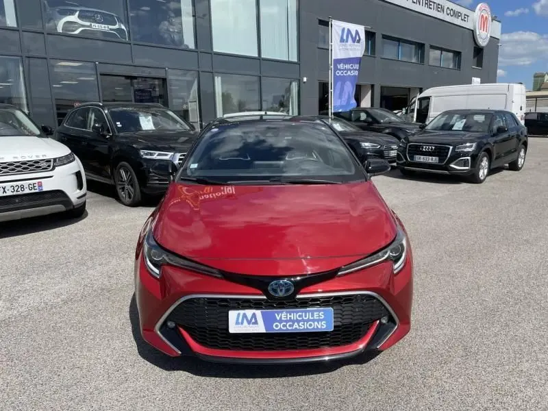 Vue frontale d'une Toyota Corolla 184 H Collection rouge métallisé avec toit noir, stationnée devant un concessionnaire.