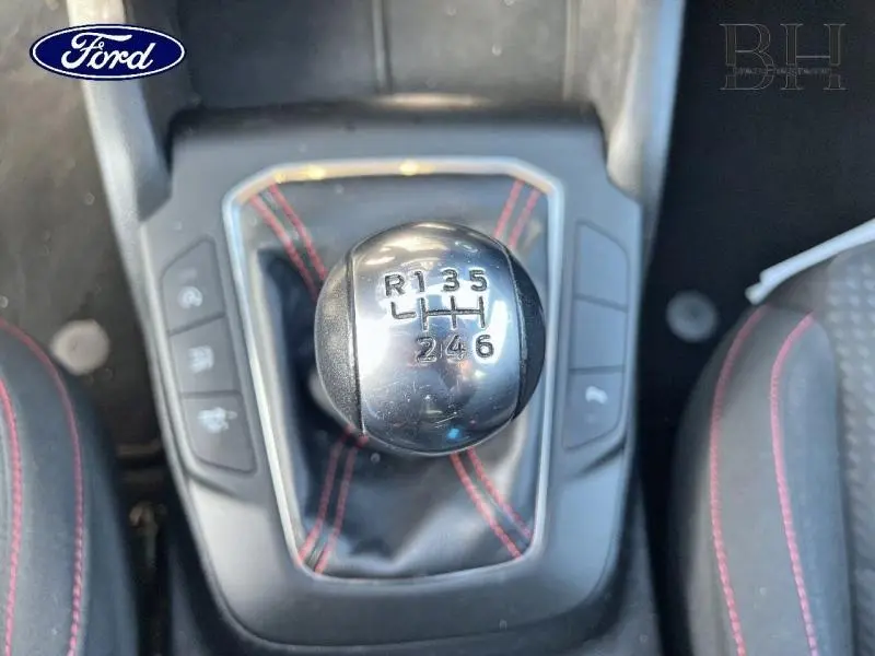 Gros plan sur le pommeau de levier de vitesse manuel de la Ford Focus gris lunaire, avec coutures rouges visibles.