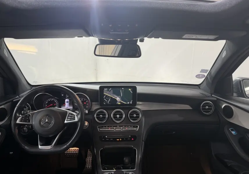 Vue intérieure avant du tableau de bord noir d'une Mercedes GLC 250 Fascination 4Matic avec écran central et volant cuir.
