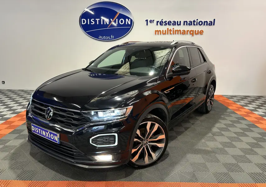 Volkswagen T-Roc noir en 3/4 avant droit, avec jantes alliage bicolores et feux LED allumés en intérieur showroom.