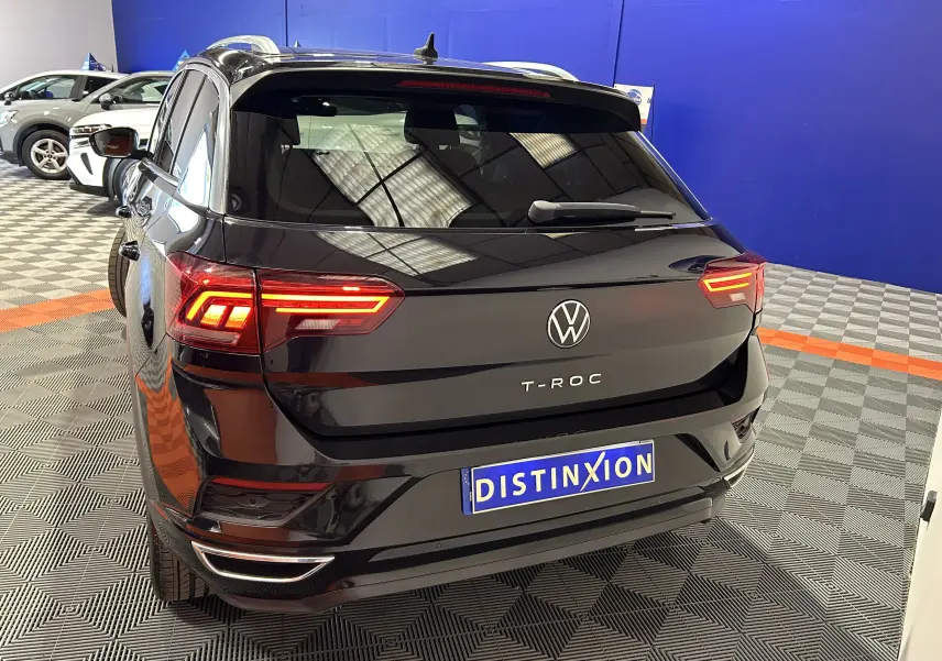 Vue 3/4 arrière d’un Volkswagen T-Roc noir avec feux arrière allumés dans un showroom.