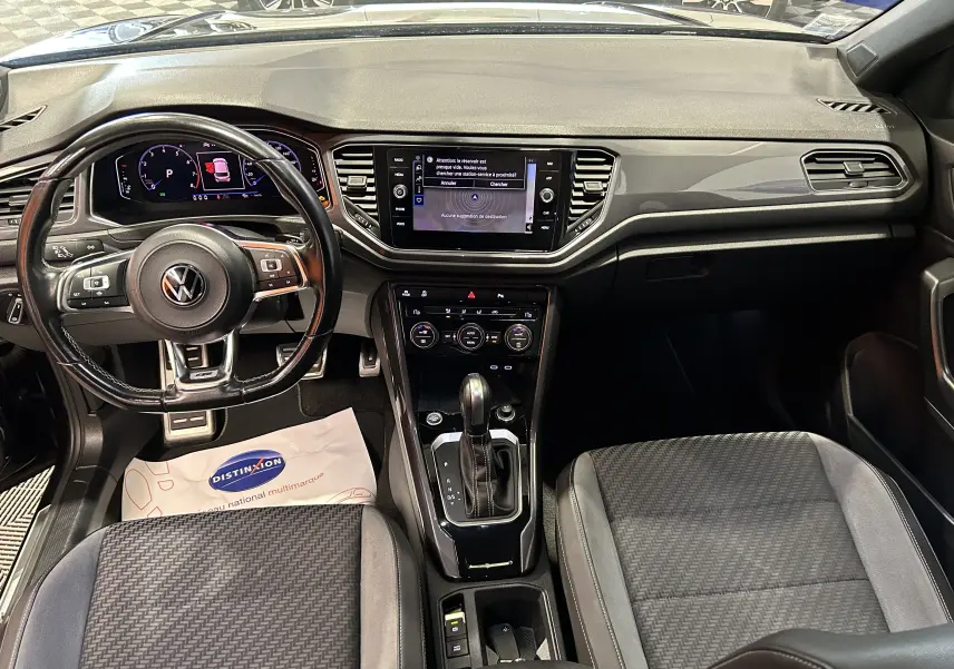 Vue intérieure du tableau de bord et volant noir du Volkswagen T-Roc TSI 150ch R-Line avec écran tactile central et console automatique.