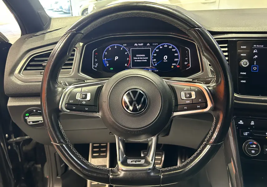 Vue centrée sur le volant noir en cuir du Volkswagen T-Roc 2020 avec tableau de bord numérique et commandes intégrées.