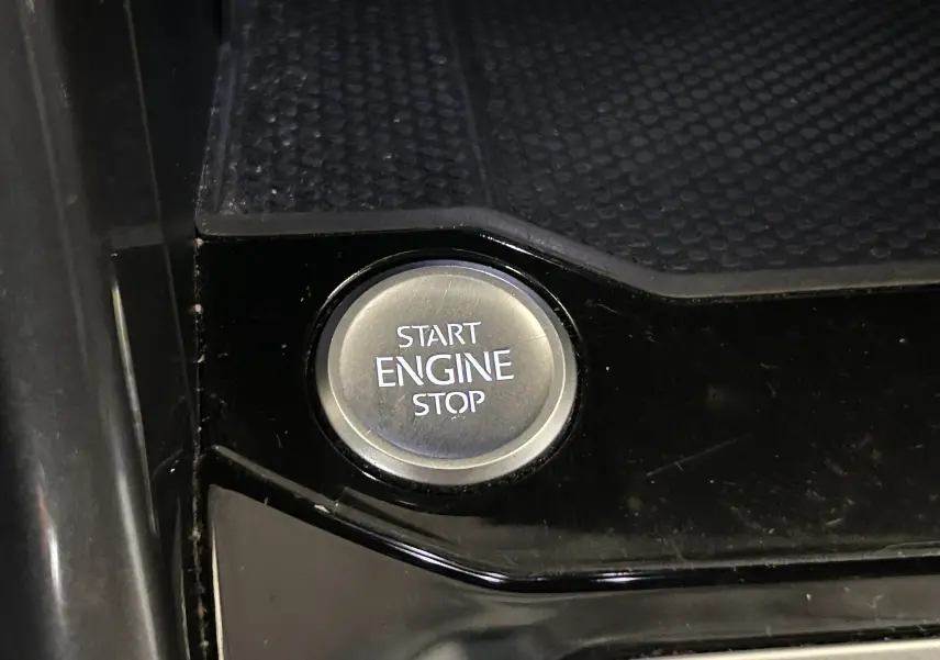 Bouton rond Start Engine Stop en gros plan sur console noire brillante d'un Volkswagen T-Roc noir.