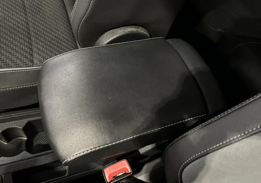Détail de l'accoudoir central en cuir noir avec surpiqûres blanches dans l'habitacle d'un Volkswagen T-Roc noir.