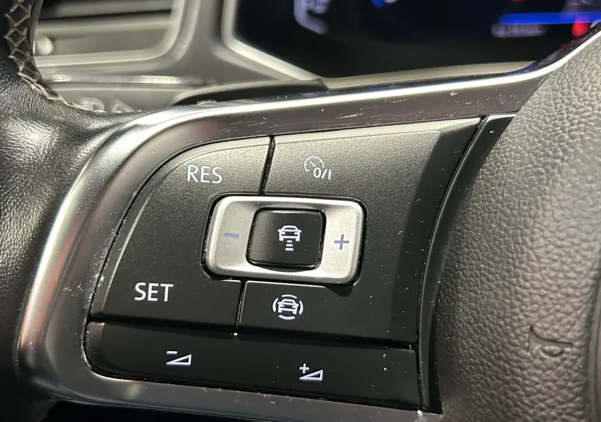 Gros plan sur les commandes noires du régulateur de vitesse au volant du Volkswagen T-Roc noir, version R-Line.
