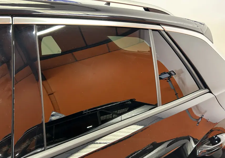 Détail de la vitre arrière côté gauche d’un Volkswagen T-Roc noir avec reflet d’éclairage intérieur.