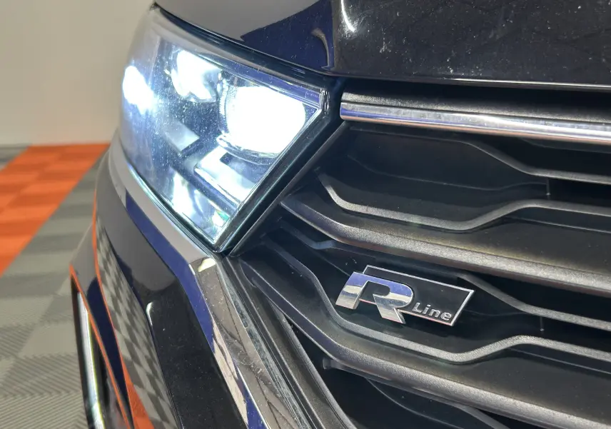 Gros plan sur le phare avant gauche et la calandre noire du Volkswagen T-Roc R-Line avec logo R visible.