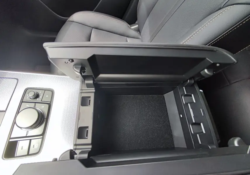 Gros plan sur la console centrale ouverte du Mazda CX-60 blanc métal, montrant un espace de rangement vide et les commandes proches.