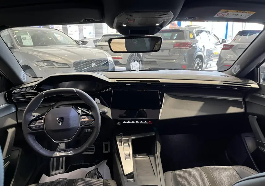 Vue intérieure avant du Peugeot 308 SW 2025 avec tableau de bord noir, volant compact et écran tactile central.