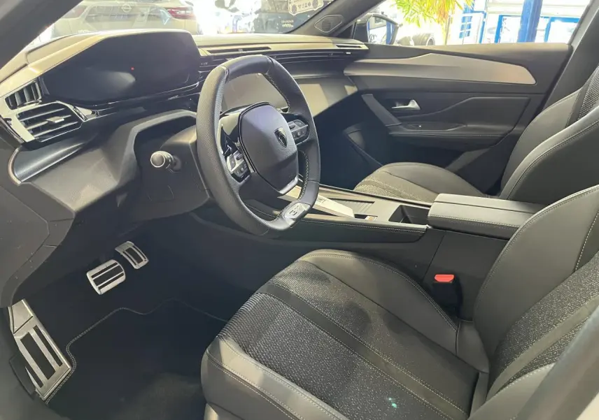 Intérieur avant droit de la Peugeot 308 SW GT 2025 avec sièges noirs et volant cuir multifonction.