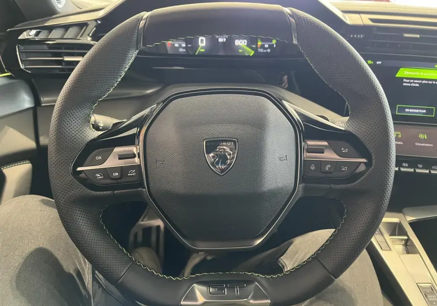Vue rapprochée du volant cuir noir perforé avec surpiqûres vertes et badge GT de la Peugeot 308 SW 2025.