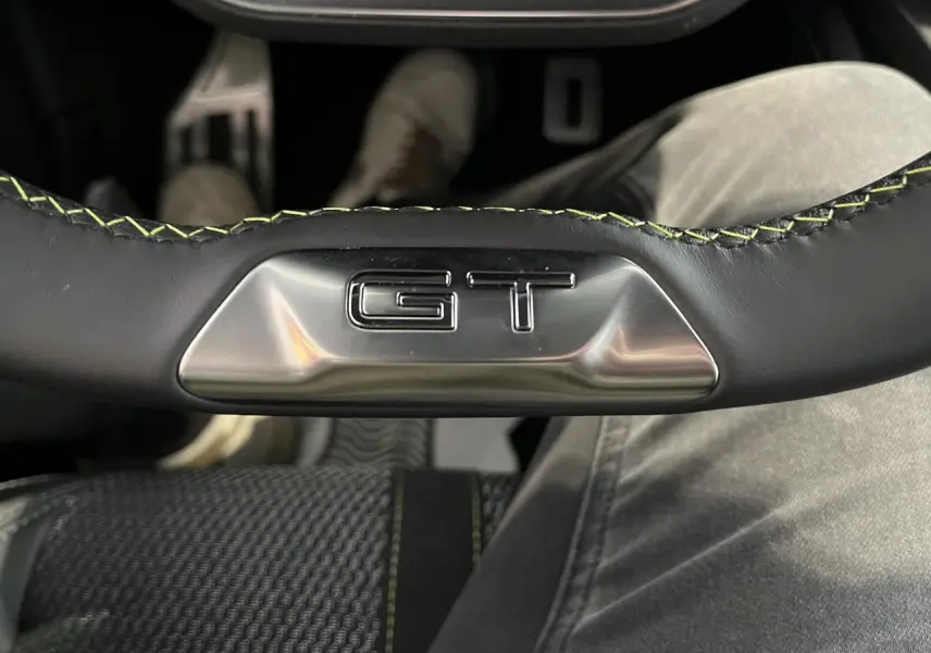 Gros plan sur le volant cuir noir avec surpiqûres vertes et logo GT en métal du Peugeot 308 SW 2025.