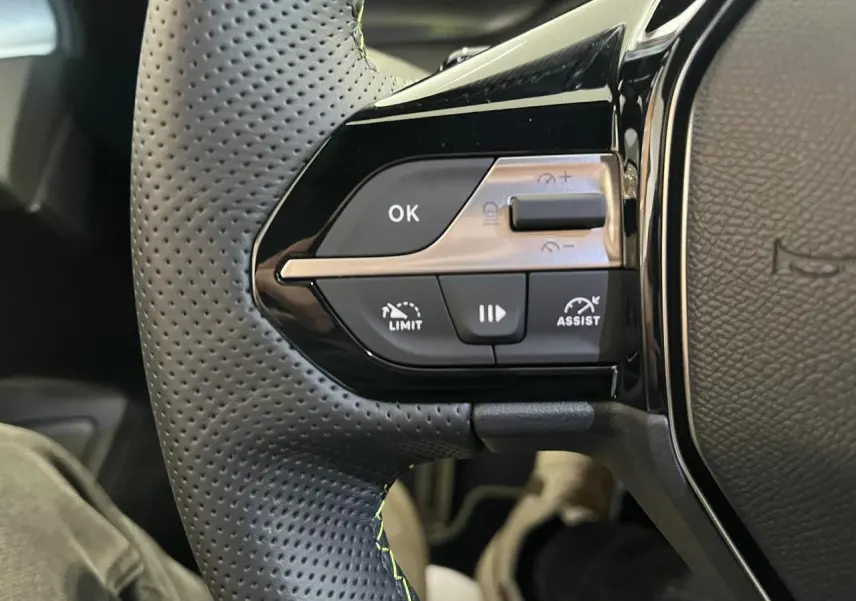 Gros plan sur les commandes à gauche du volant cuir perforé du Peugeot 308 SW blanc okenite 2025.