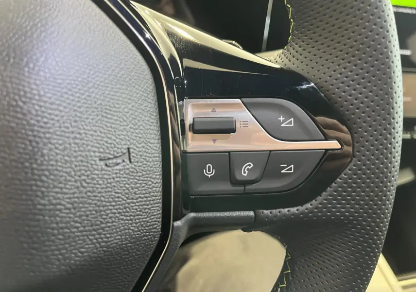 Gros plan sur les commandes du volant cuir perforé de la Peugeot 308 SW GT 2025, finition noire avec surpiqûres vertes.