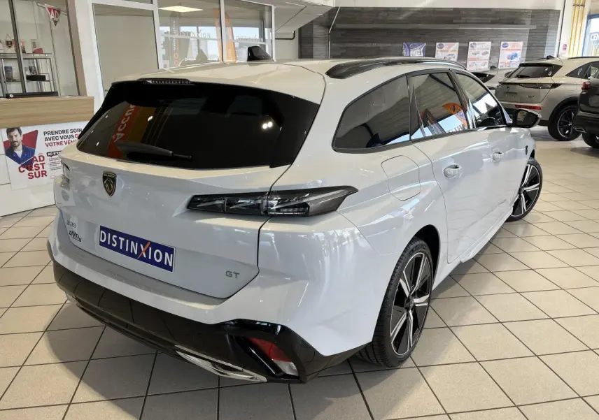 Peugeot 308 SW GT blanc okenite vue 3/4 arrière droit en intérieur avec jantes alliage et vitres surteintées.