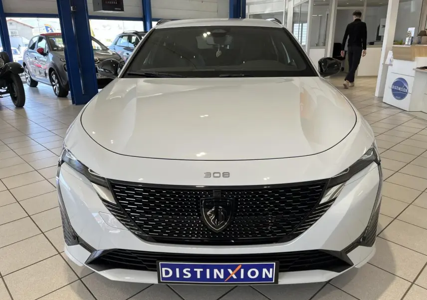 Vue frontale d'une Peugeot 308 SW blanche Okenite avec calandre noire brillante et logo lion au centre.